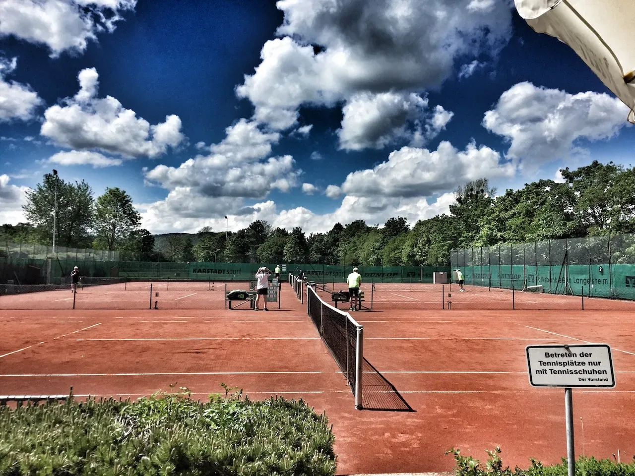 Die Freiluft-Sandplätze der Tennisabteilung des MTV Astfeld an einem sonnigen Tag, mehrere Spieler auf den Plätzen.